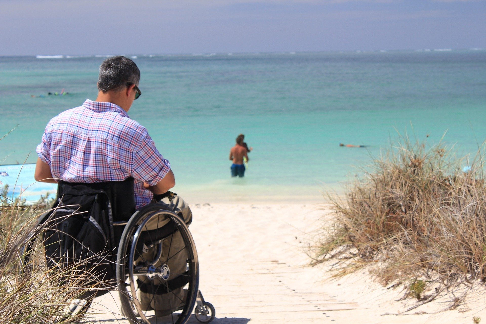 Mann im Rollstuhl blickt auf den Strand und das Meer